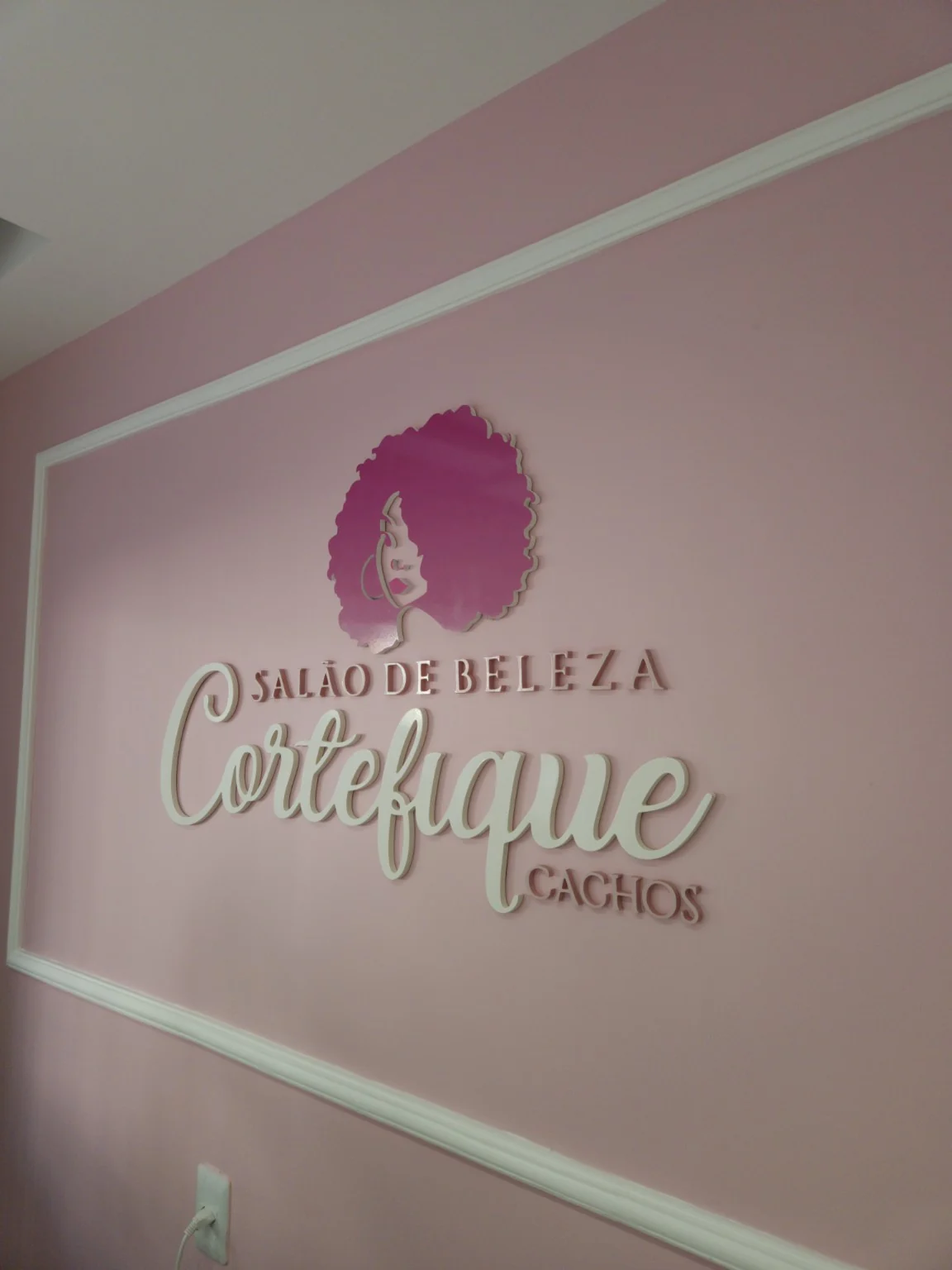 Identidade visual e letras em relevo na parede do salão de beleza.